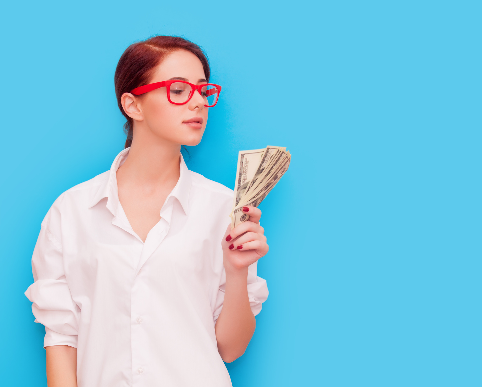 Portrait of redhead woman in red glasses with money on blue background