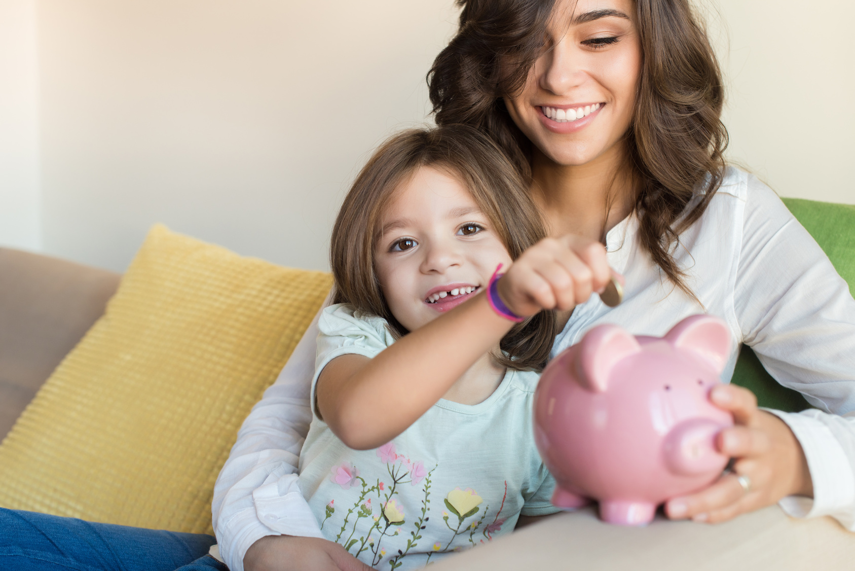 Mother and daughter putting coins into piggy bank