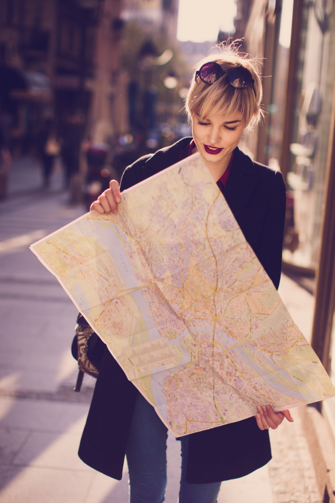 Young beautiful female traveler standing on the street and looking at the map