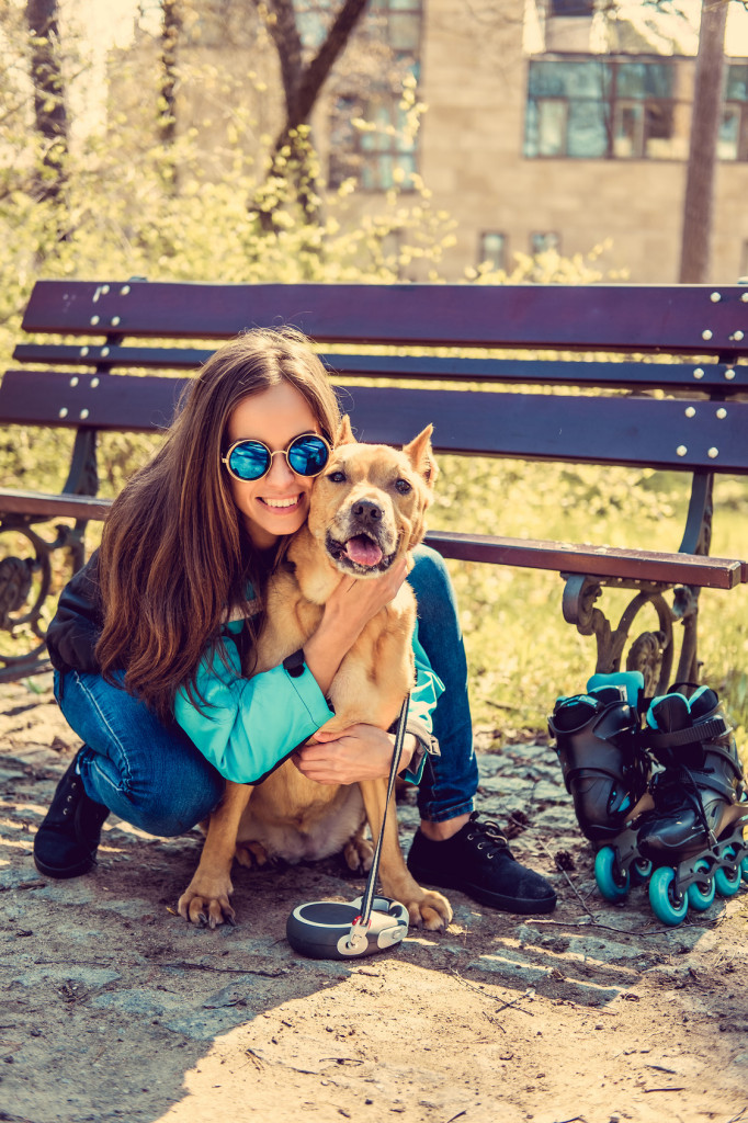 Smiling casual female with her brown pitbull dog in a park.