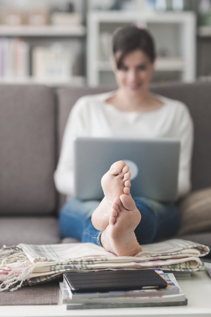 Young woman at home relaxing on the couch, she is using a laptop, feet up on the foreground