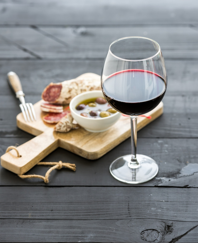 Wine appetizer set. Glass of red wine, French sausage and olives on black wooden backdrop, selective focus