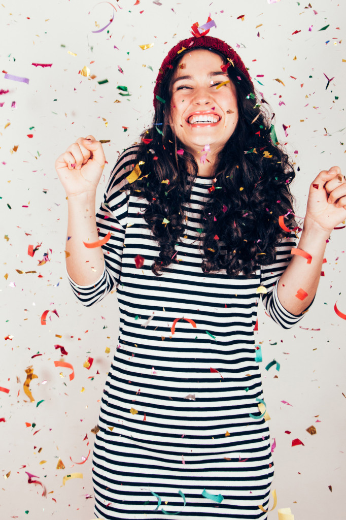 Laughing girl with striped dress and wool cap under a rain of confetti. Filter effect added. Filter effect added.